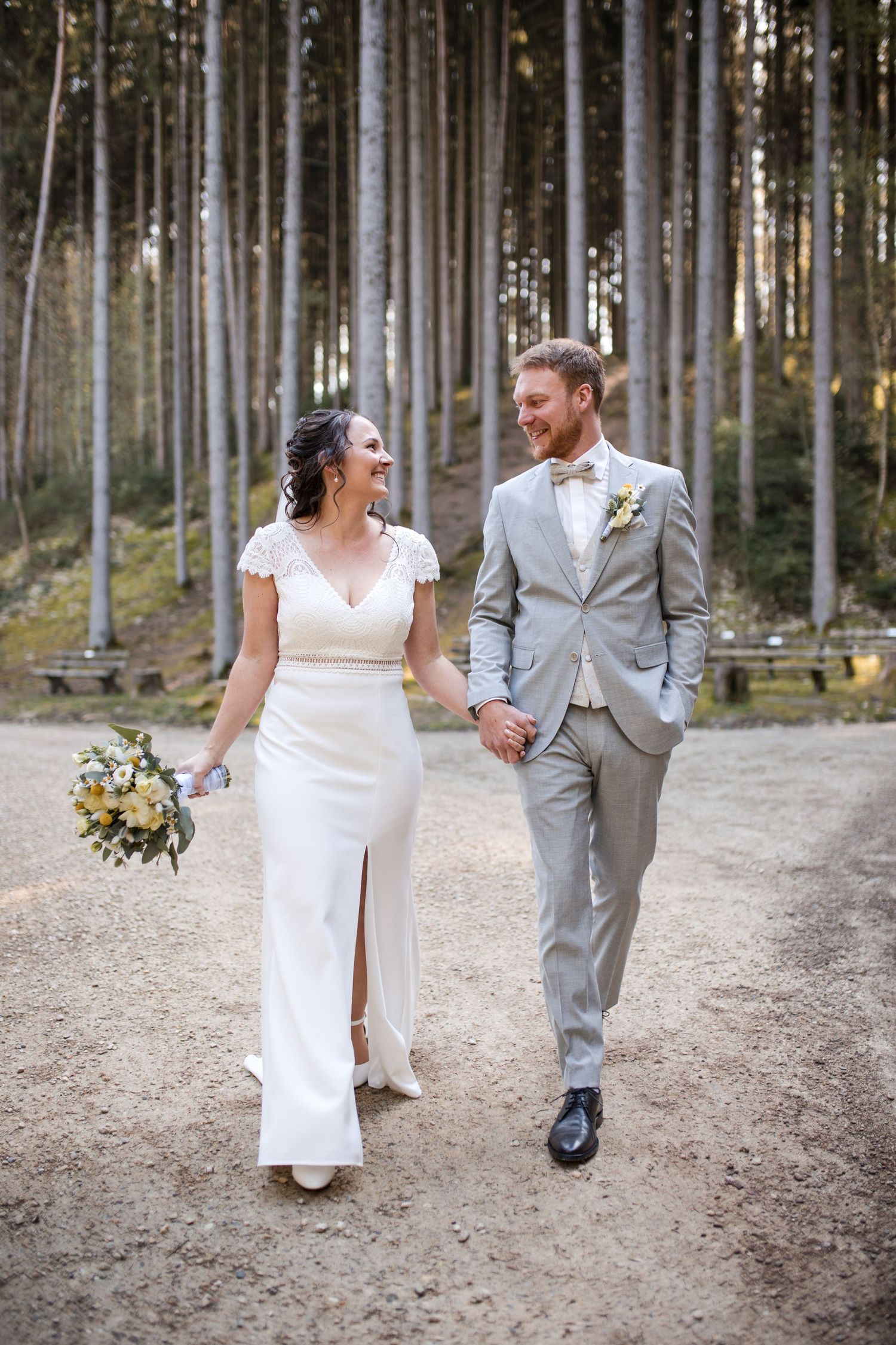 Joyful couple walking hand in hand through tall forest trees.