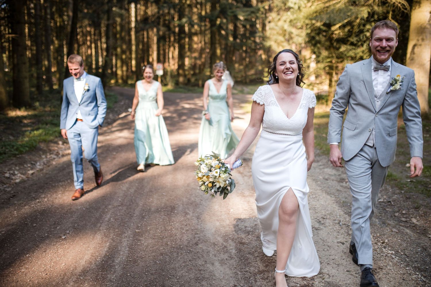 Wedding party walking and laughing together on a forest path.