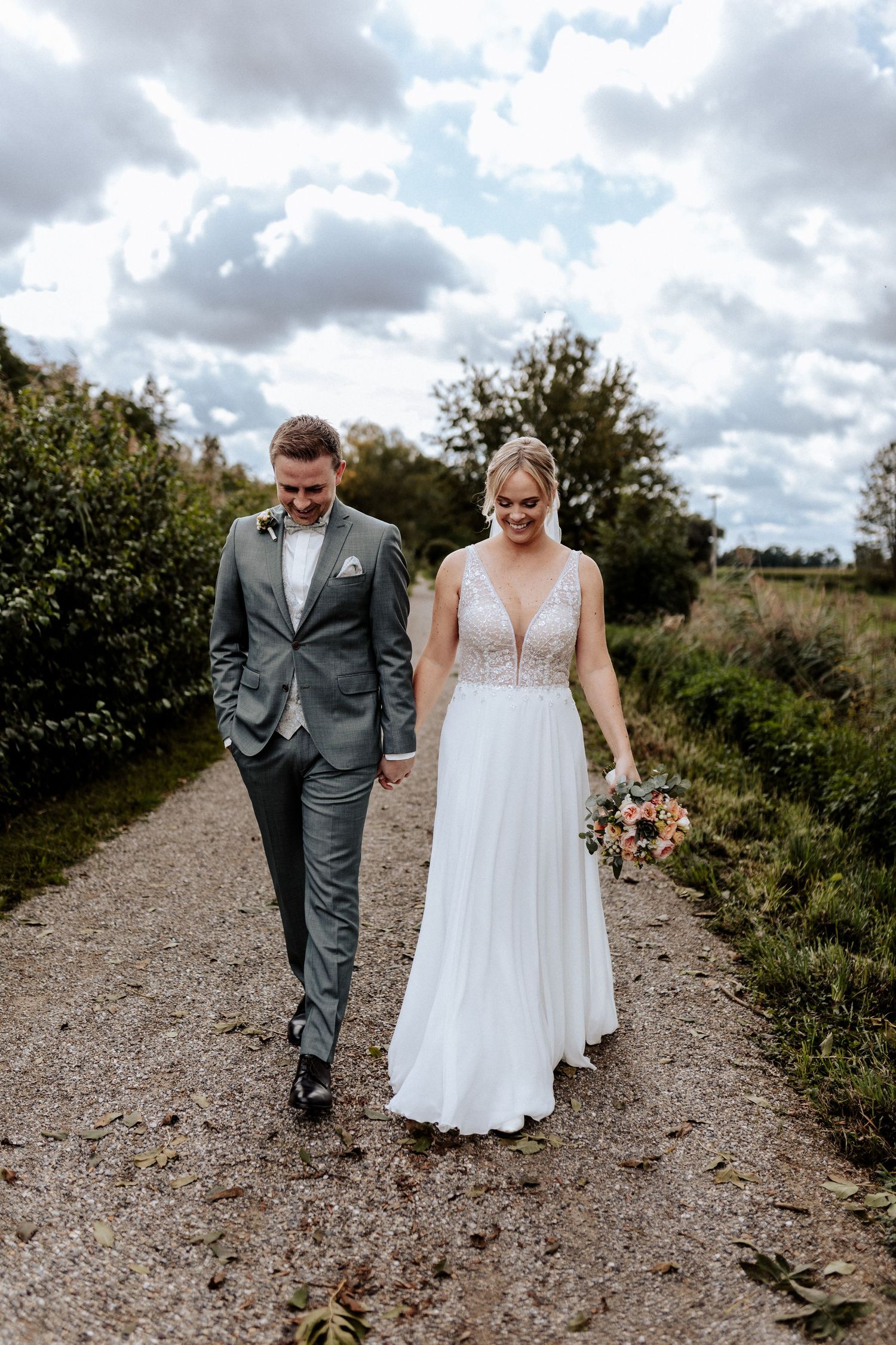Couple walking together on a gravel path under dramatic cloudy skies.