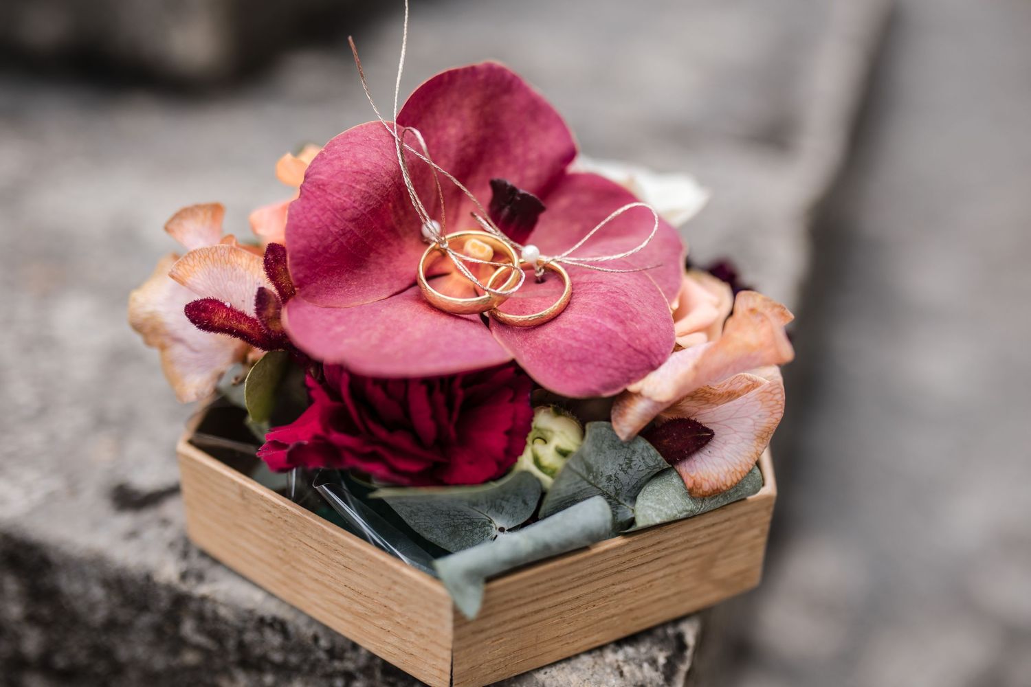 Wedding rings displayed on pink orchid flower in vintage wooden box.