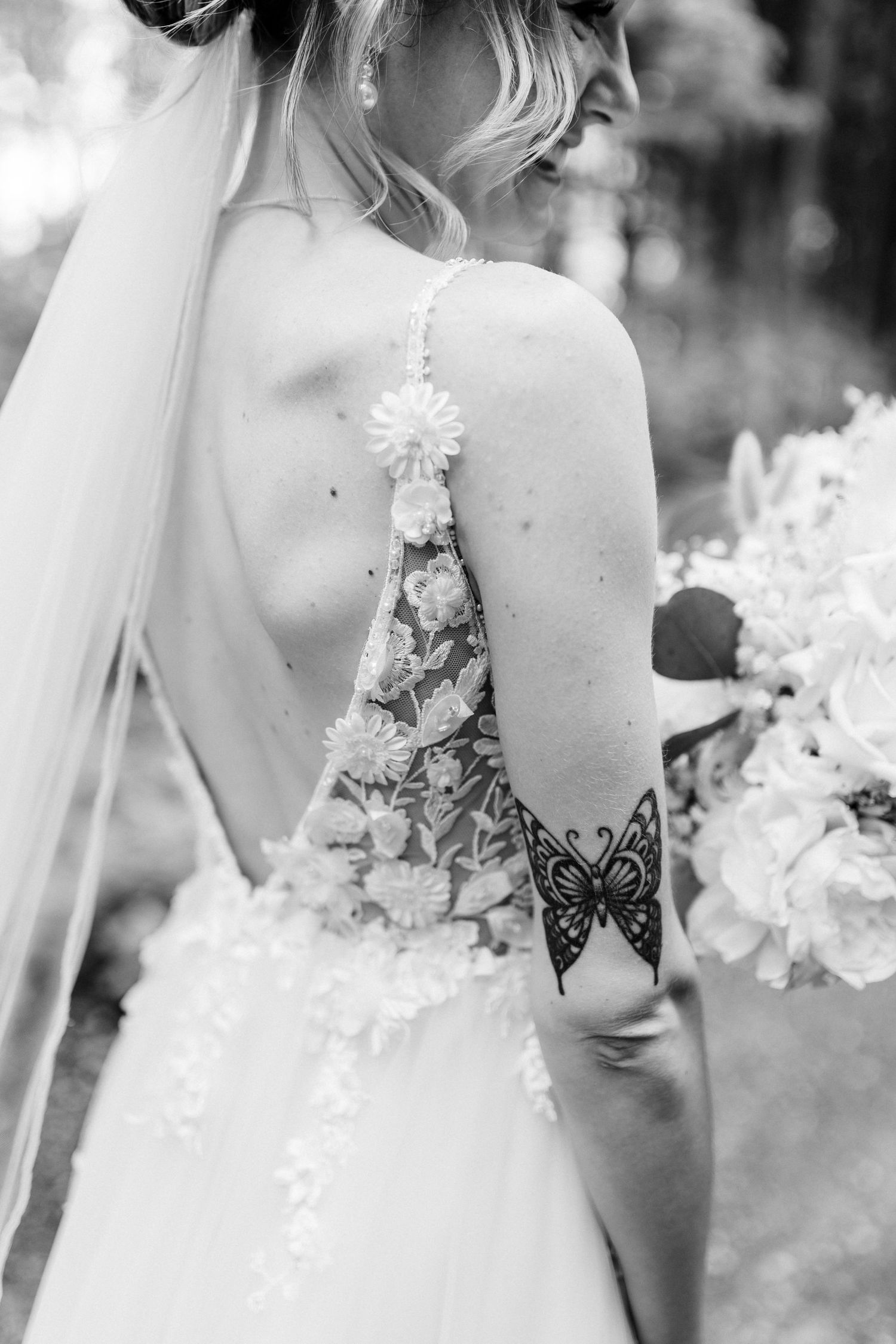 Black and white detail shot of bride's lace back wedding dress and butterfly tattoo.