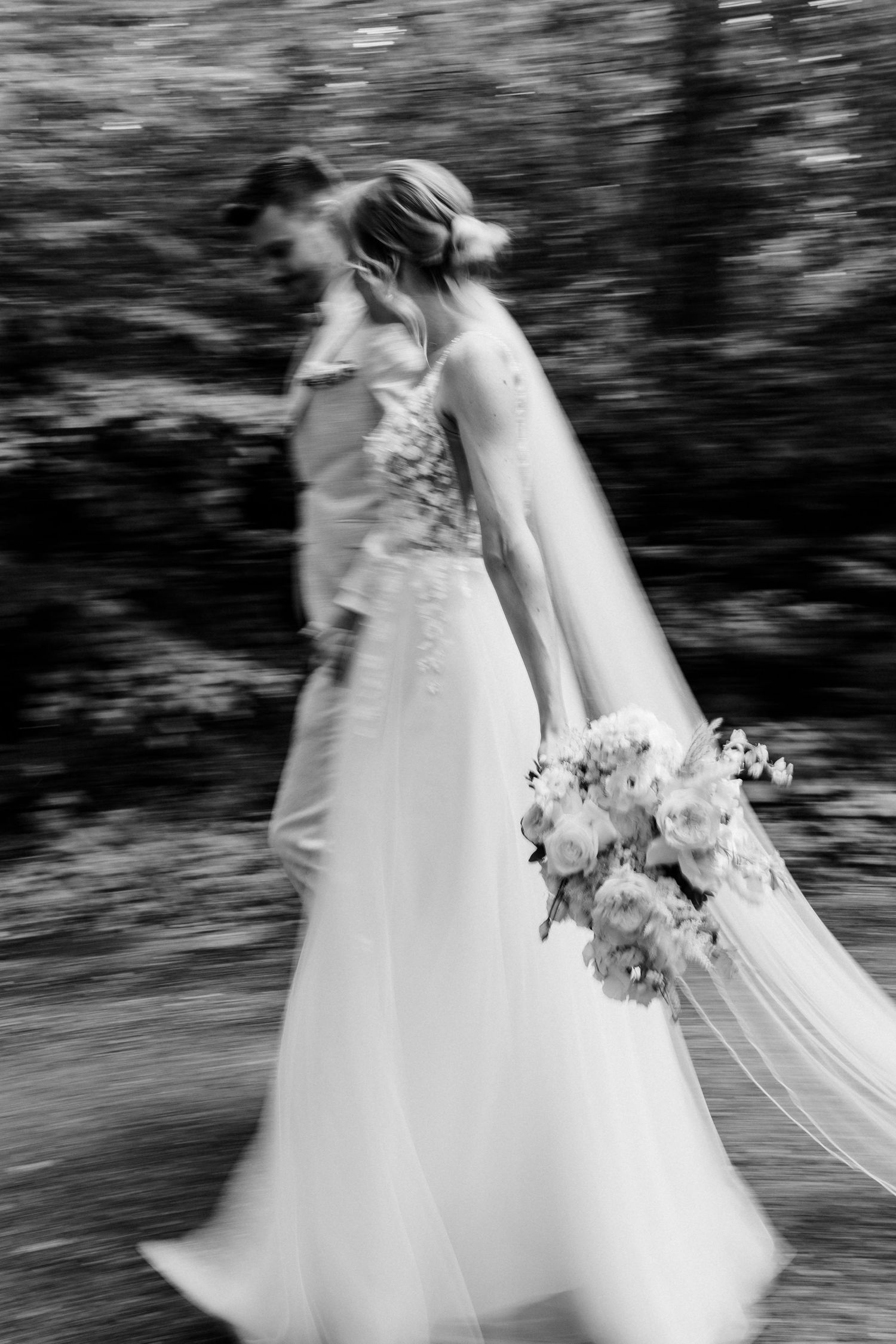 Black and white artistic motion blur photo of bride in flowing gown with bouquet.