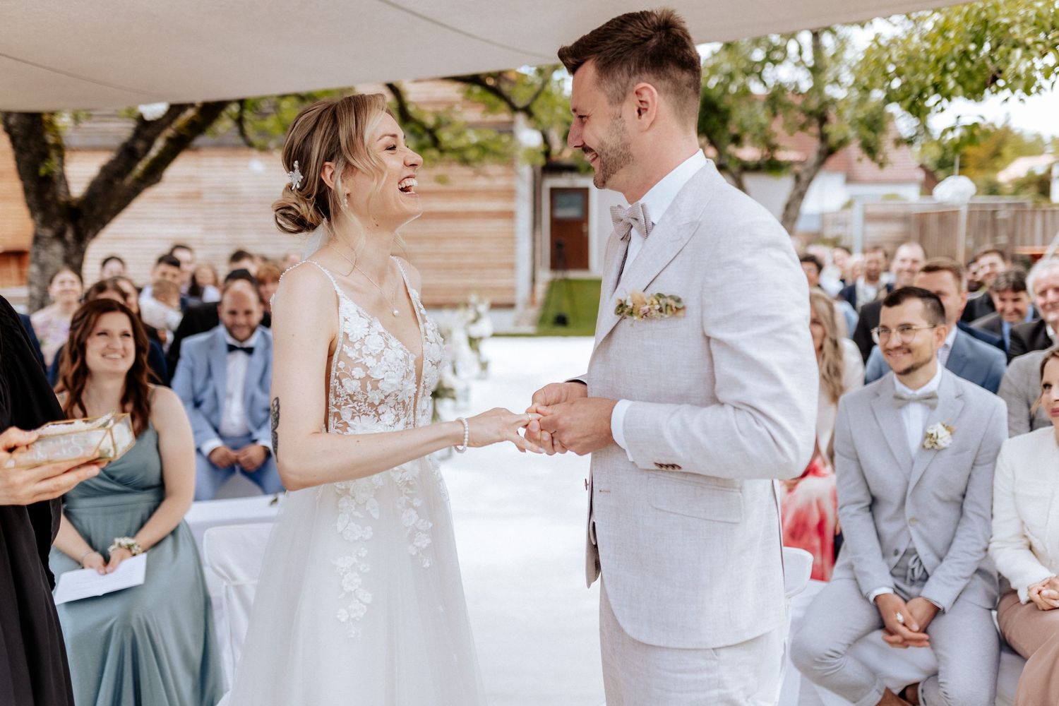 Couple exchanging rings during outdoor wedding ceremony surrounded by guests.