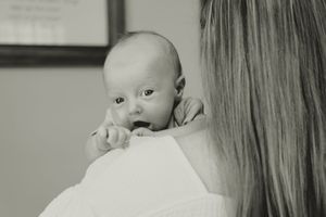 A baby peers over a parent's shoulder while being held, captured in black and white photography.