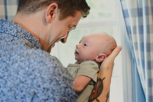 A tender moment between parent and baby against a bright window backdrop with blue curtains.