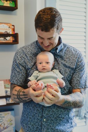 A series of four photos showing someone in a blue floral shirt holding and interacting with a small baby.