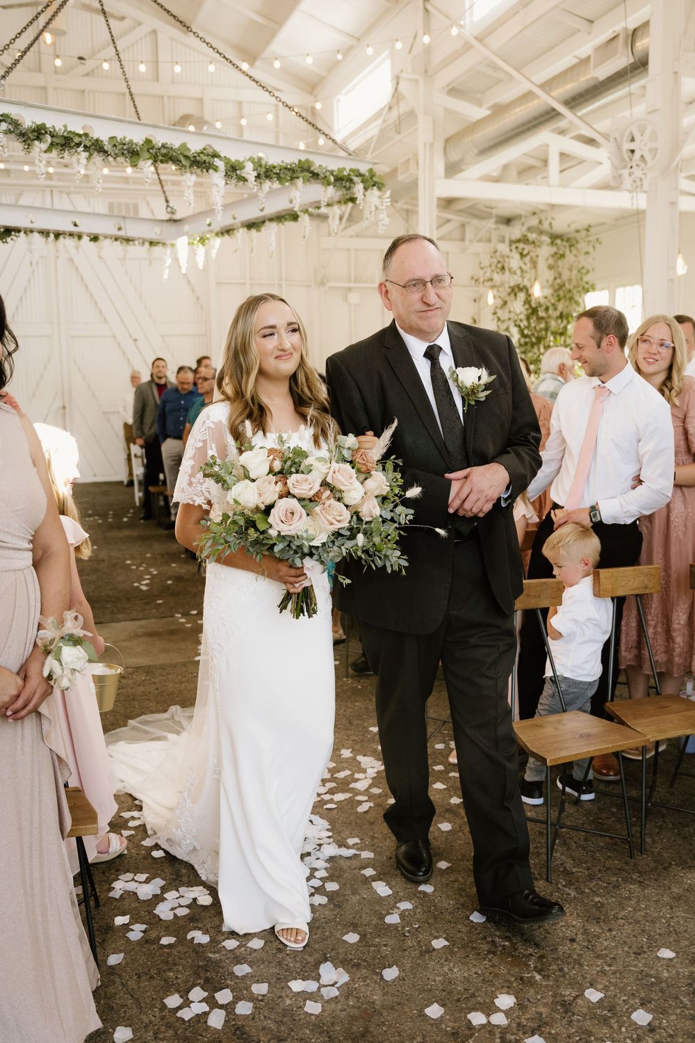 Wedding ceremony processional in bright industrial venue with floral decorations.