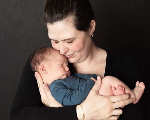 Caring embrace between parent and newborn baby against dark backdrop in tender studio portrait.nyfødtfotografering lillestrøm romerike