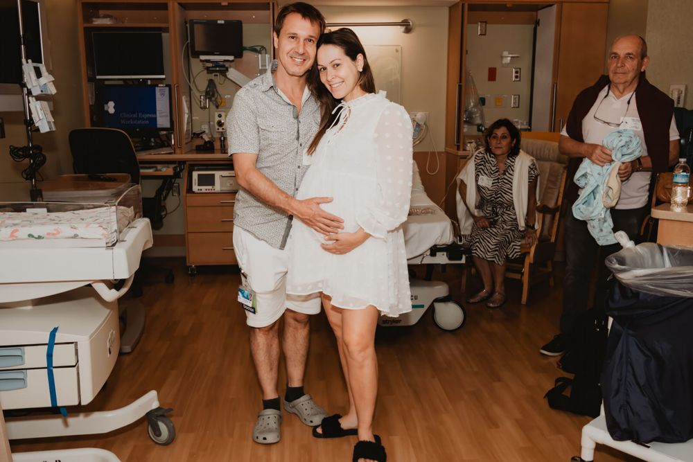 Couple standing together in hospital room with medical equipment visible.
