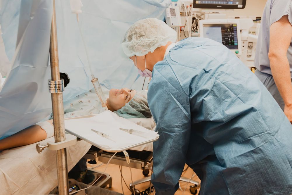 Medical staff in surgical attire tend to a patient on an operating table during a medical procedure.