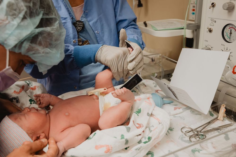 Medical staff in blue scrubs examines newborn baby in hospital setting.