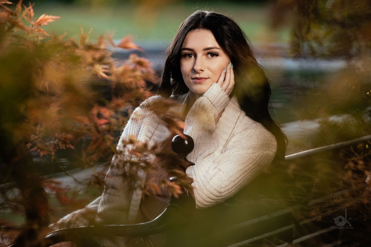 A person in a cream sweater poses outdoors during autumn with warm bokeh and fall foliage in the foreground.
