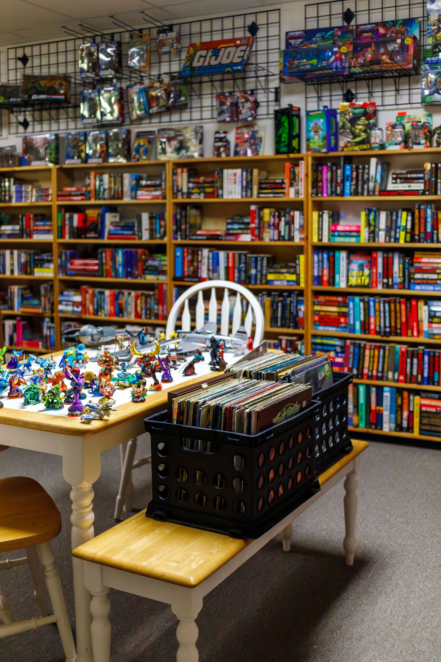 Wooden table displaying colorful toys and collectibles in front of bookshelves filled with comics and graphic novels.