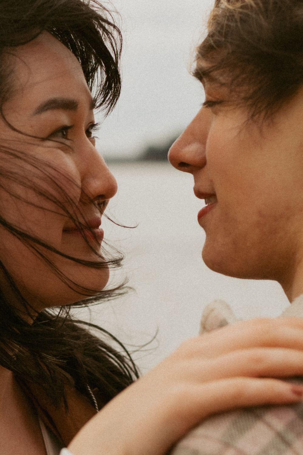 Couple sharing an intimate moment with wind-blown hair against overcast sky.