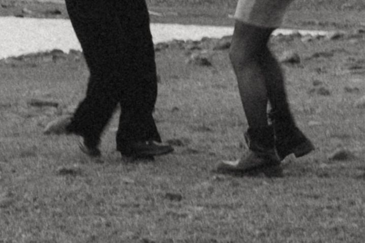 Silhouetted legs walking across a dark grassy field.