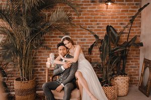 Romantic indoor photo shoot with exposed brick wall, palm plants, and vintage decor creating an intimate atmosphere.