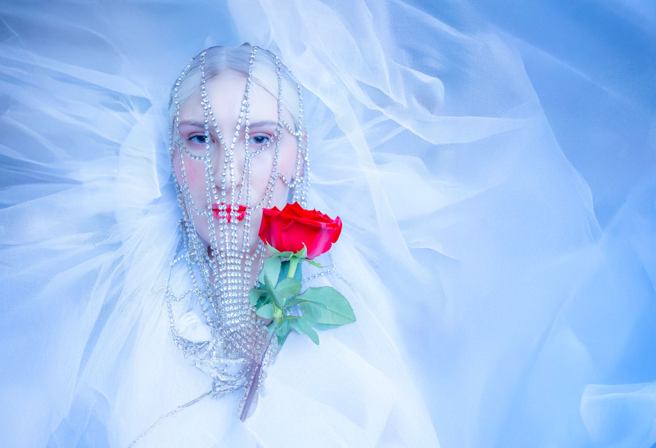Ethereal portrait with a red rose against flowing white fabric and delicate mesh details.