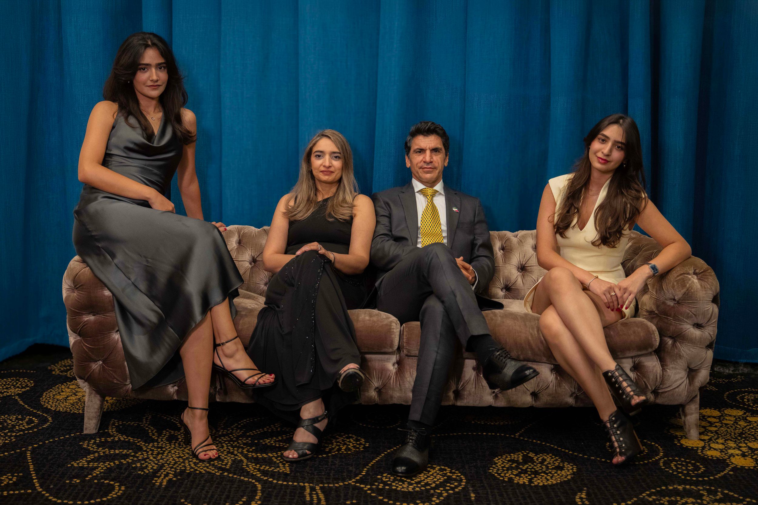 Group lounging on floor against blue curtain backdrop in casual setting.