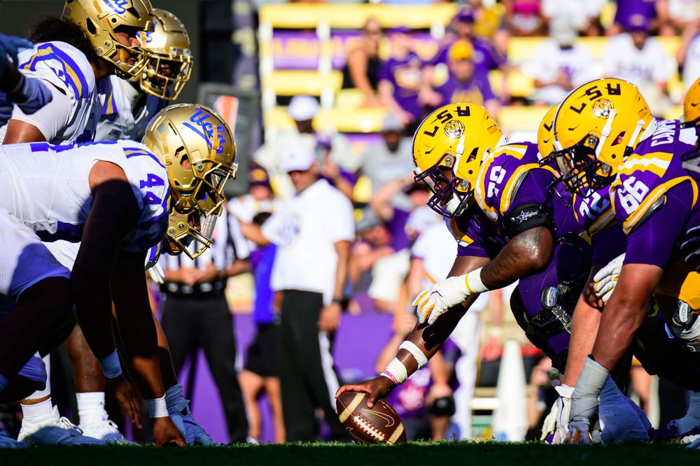 Football players lined up at scrimmage during game with purple and gold uniforms.