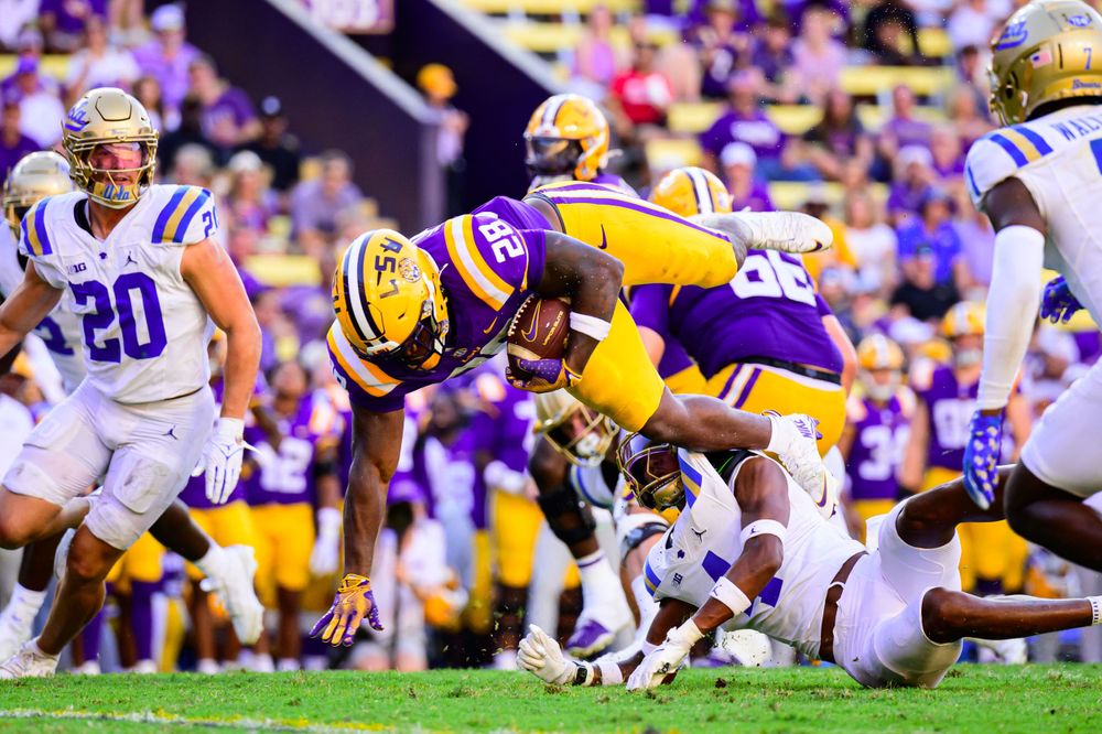 Line of scrimmage view of football players in LSU and opposing team uniforms ready for play.