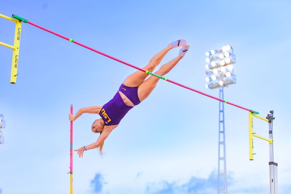 Track and field athlete performs high jump attempt against blue sky background.