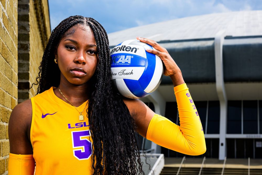 LSU athlete poses with volleyball in yellow uniform outside brick building.