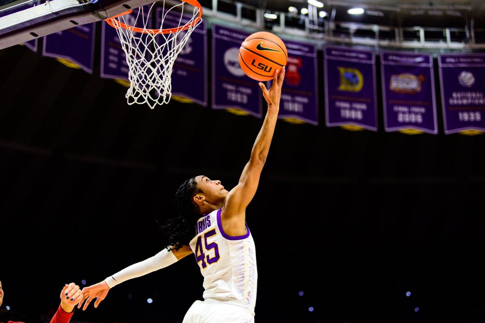 LSU basketball players compete for rebounds near the hoop in a dimly lit arena.