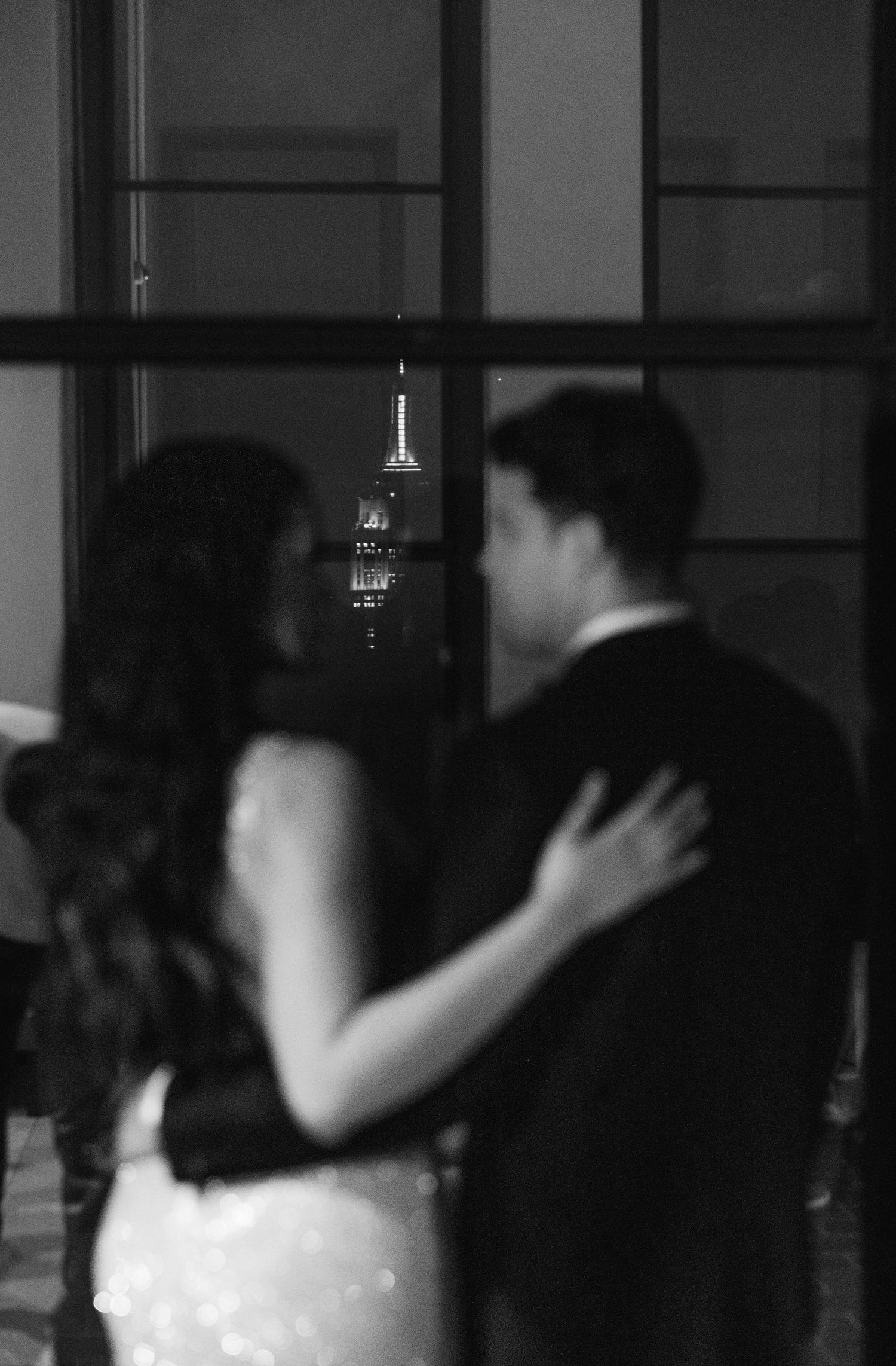 Silhouetted couple embraces with Empire State Building visible through window.