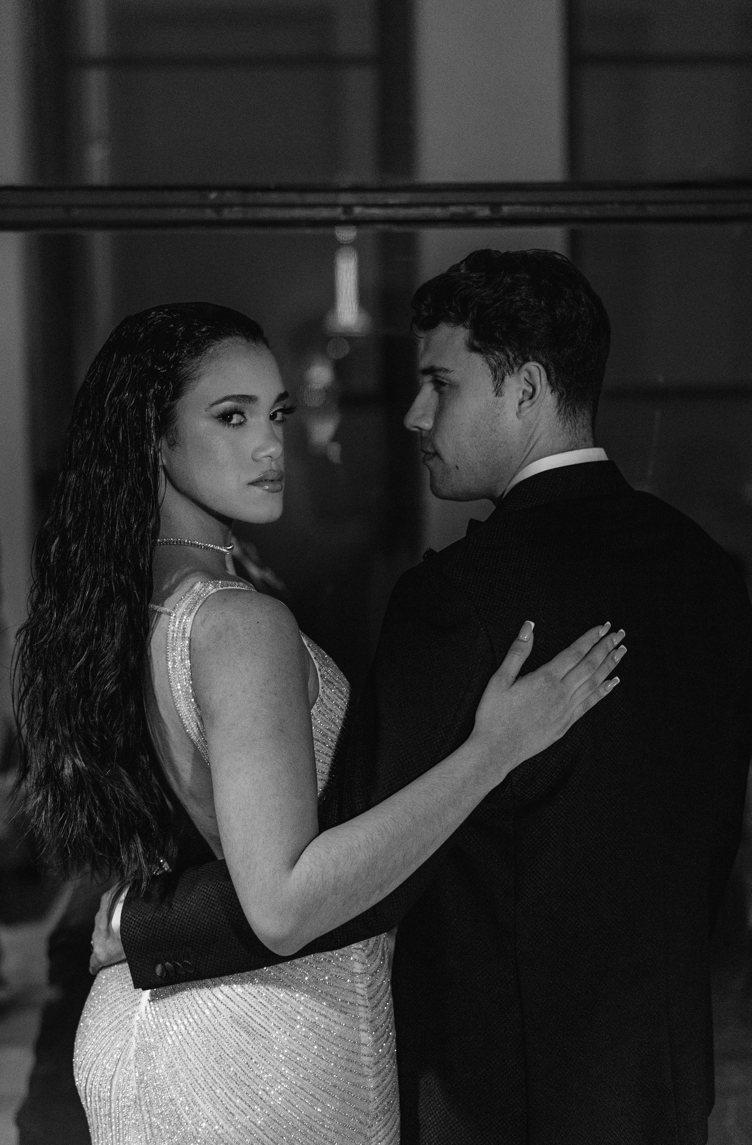 Glamorous couple in formal attire poses intimately in black and white portrait.
