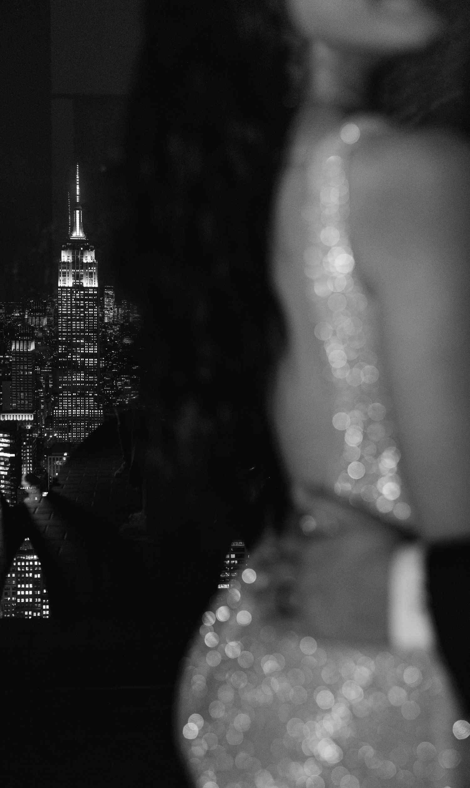 Sparkling gown catches light with Empire State Building illuminated in background.
