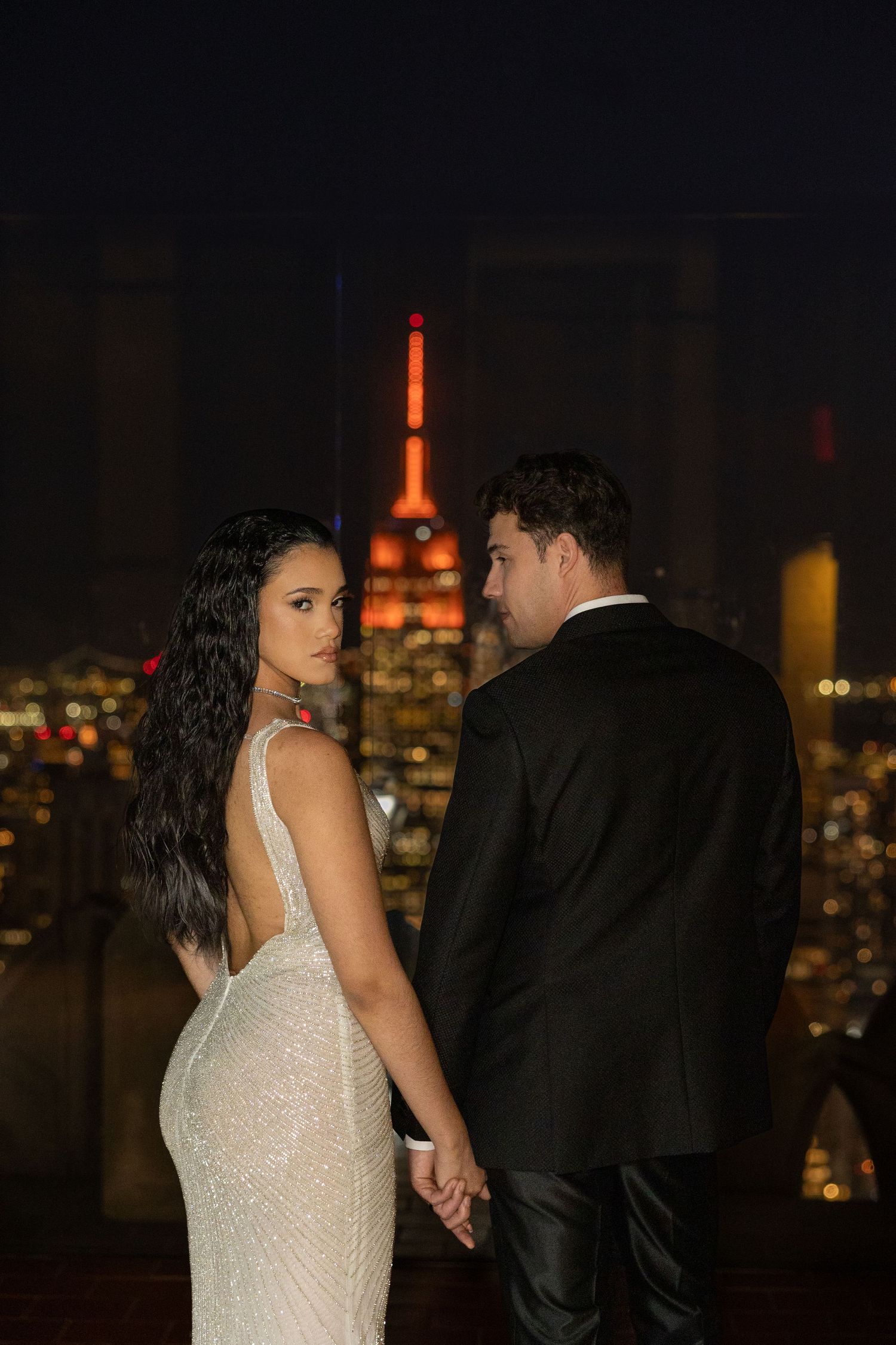 Couple shares intimate moment against backdrop of illuminated Empire State Building.