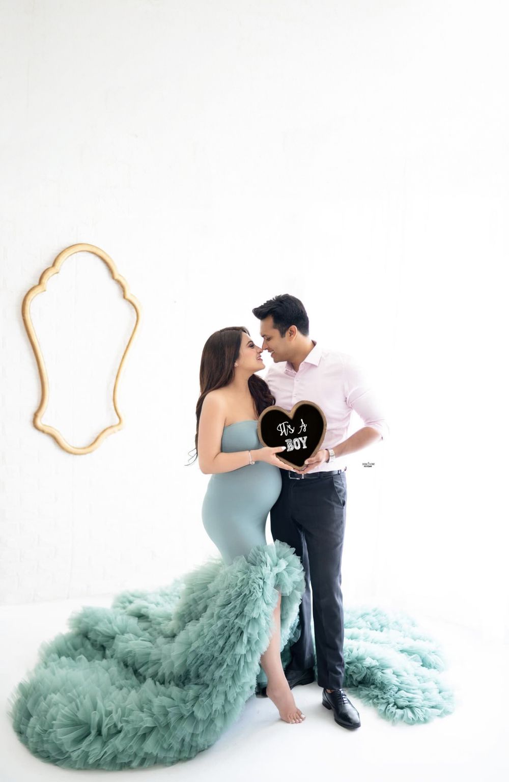 Elegant maternity portrait with couple holding heart sign, featuring mint green flowing dress.