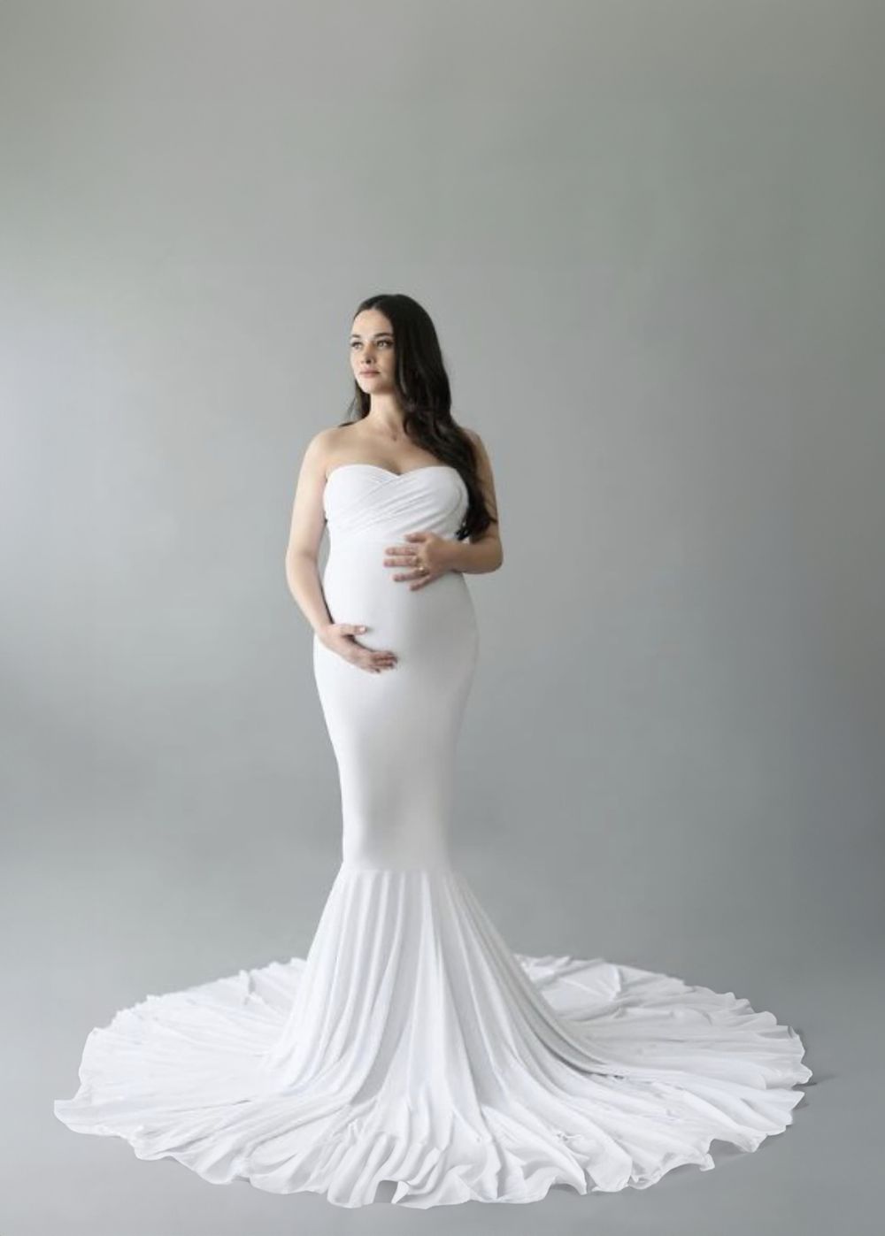 Elegant maternity portrait in fitted white mermaid gown against grey background.