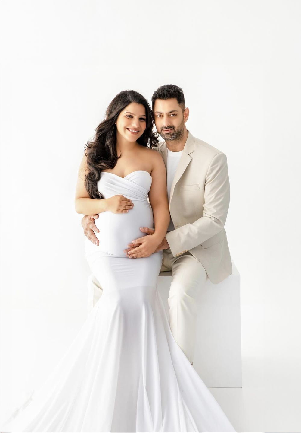 Minimalist studio maternity portrait featuring couple in white and beige formal attire.