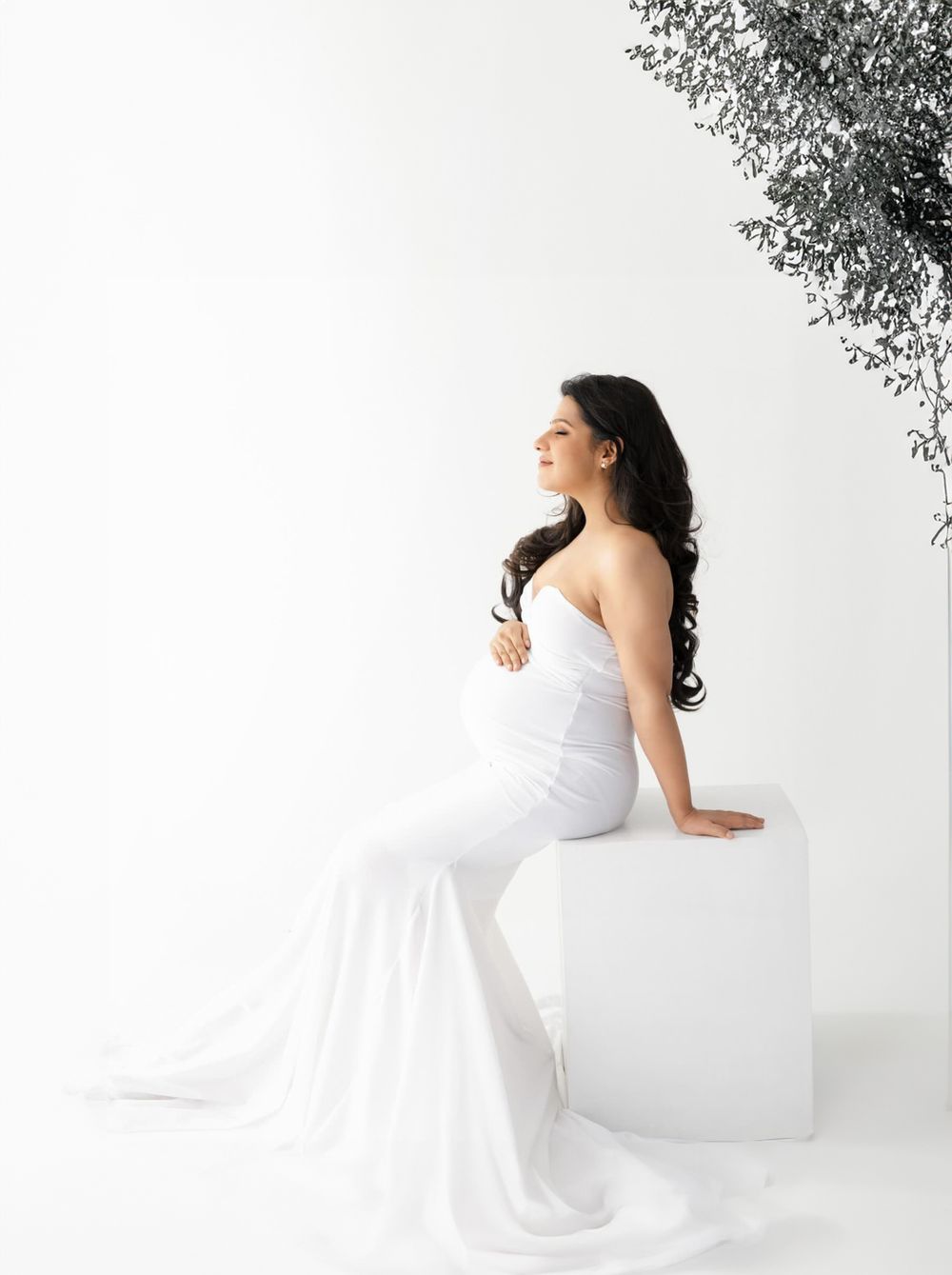 Artistic maternity portrait with figure seated on white pedestal against minimal background.