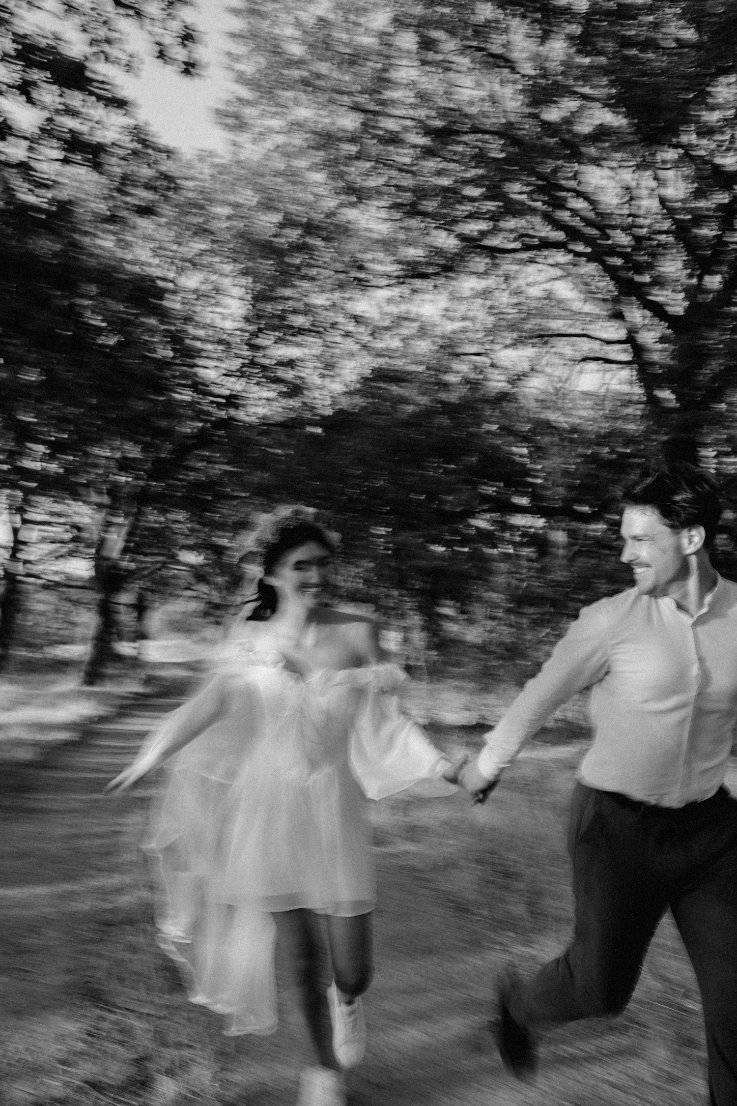 Black and white motion-blur photo of couple running through a wooded area.