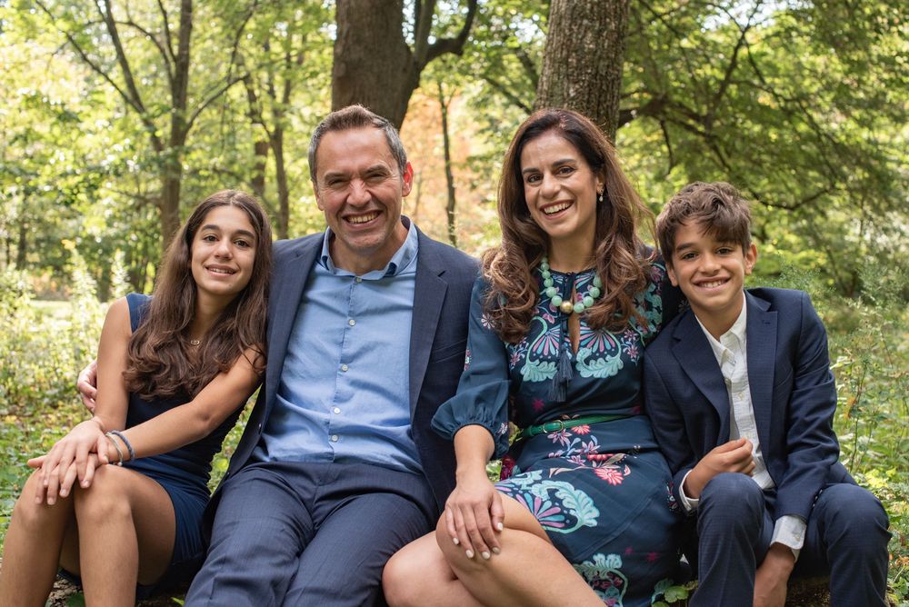 A group of people sit together on a wooden bench in a lush green outdoor setting.