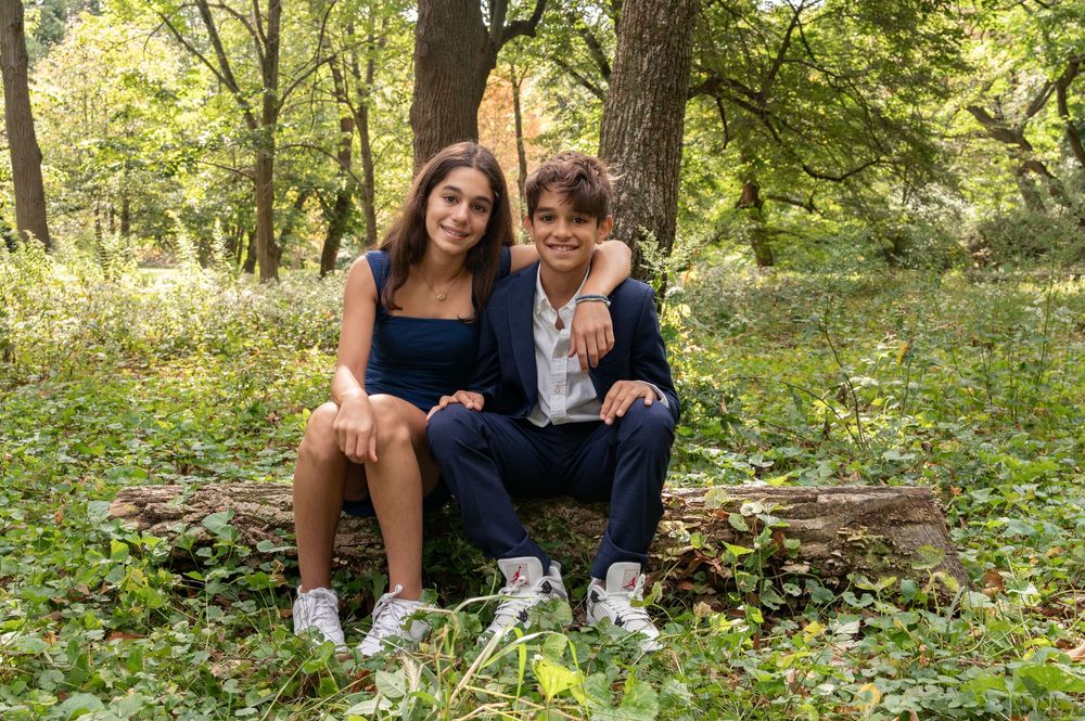 A couple sits together on stone steps surrounded by lush green foliage in a wooded outdoor setting.