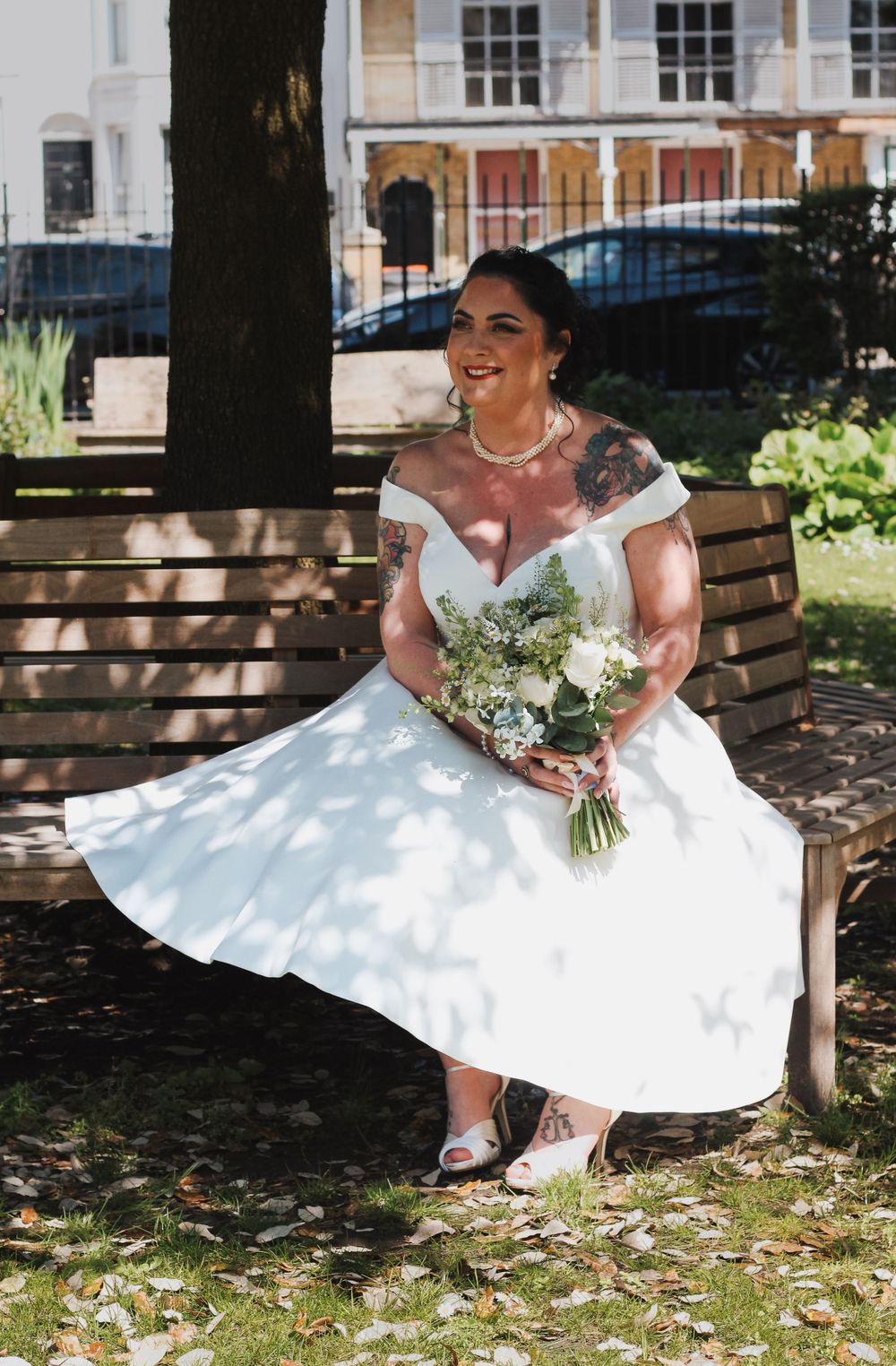 Bride sitting on a bench holding her bouquet and smiling at the camera at Portsmouth wedding captured by Shayla Bloom Photography
