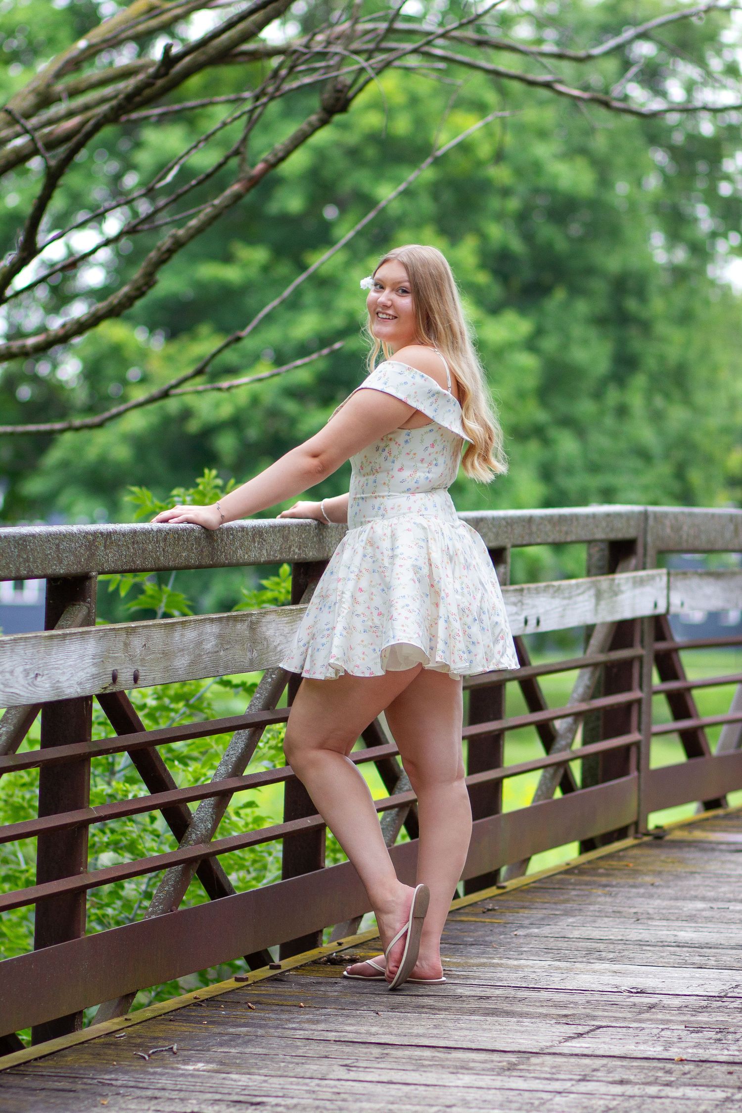 Summer fashion shoot on wooden bridge featuring flowing white dress and graceful poses.