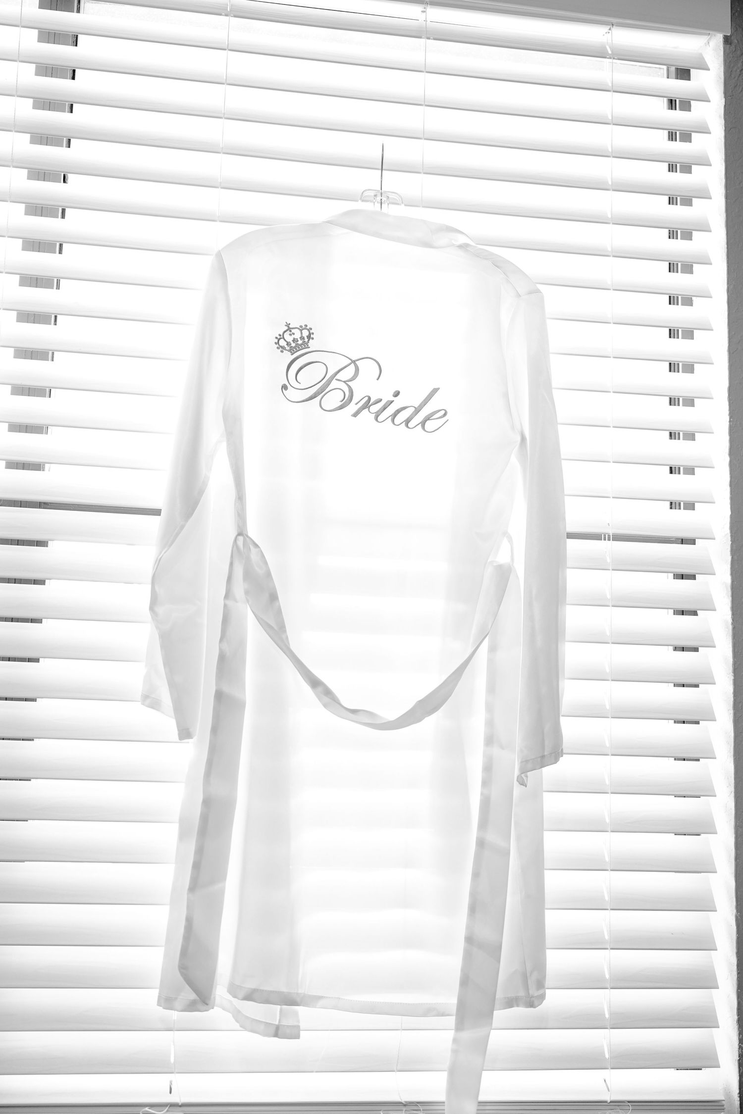 White bridal party robes hanging on display against window blinds.