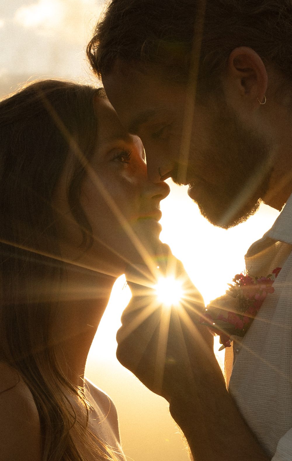 A silhouetted couple shares an intimate moment as sunbeams burst through between them during golden hour.