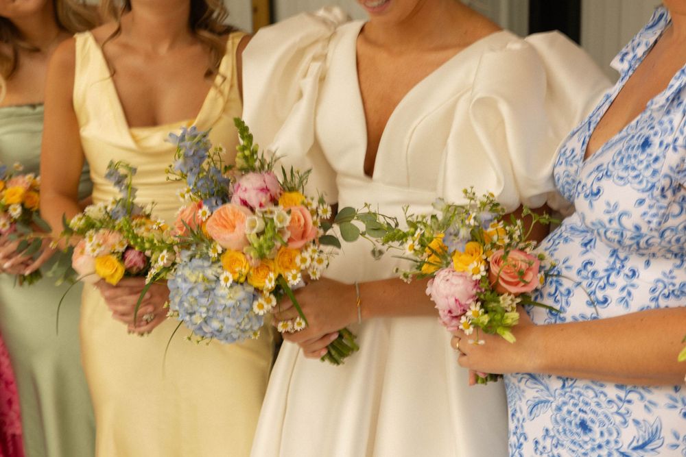 Bridesmaids holding colorful bouquets with yellow, pink, and blue flowers.