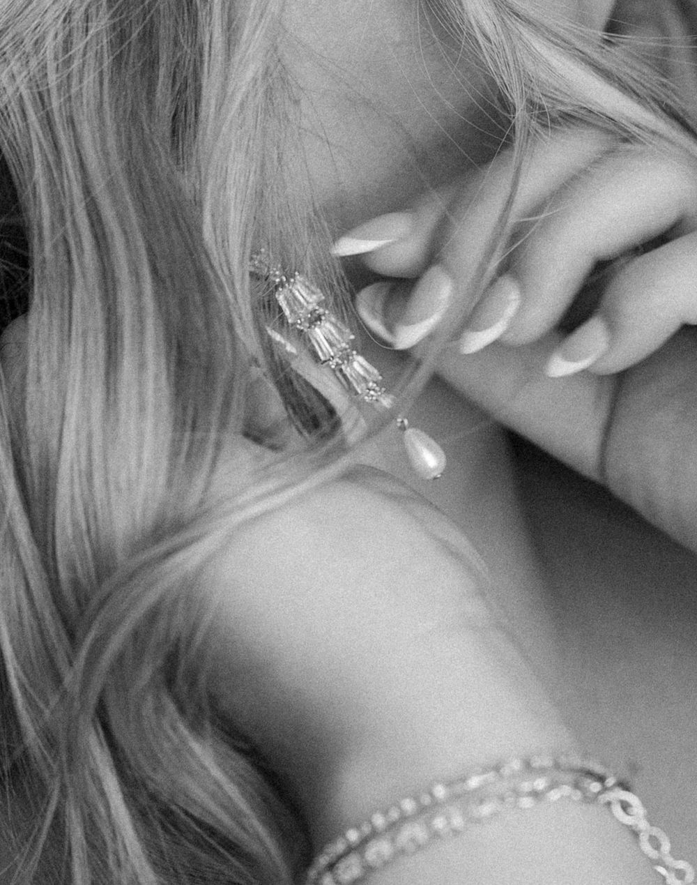 Black and white close-up image showing sparkly jewelry, blonde hair, and a delicate hand touching an ear.