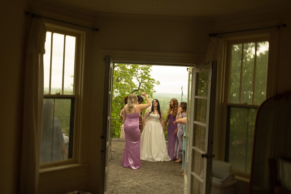 View through open French doors of three women in formal dresses walking along an outdoor garden path in soft lighting.