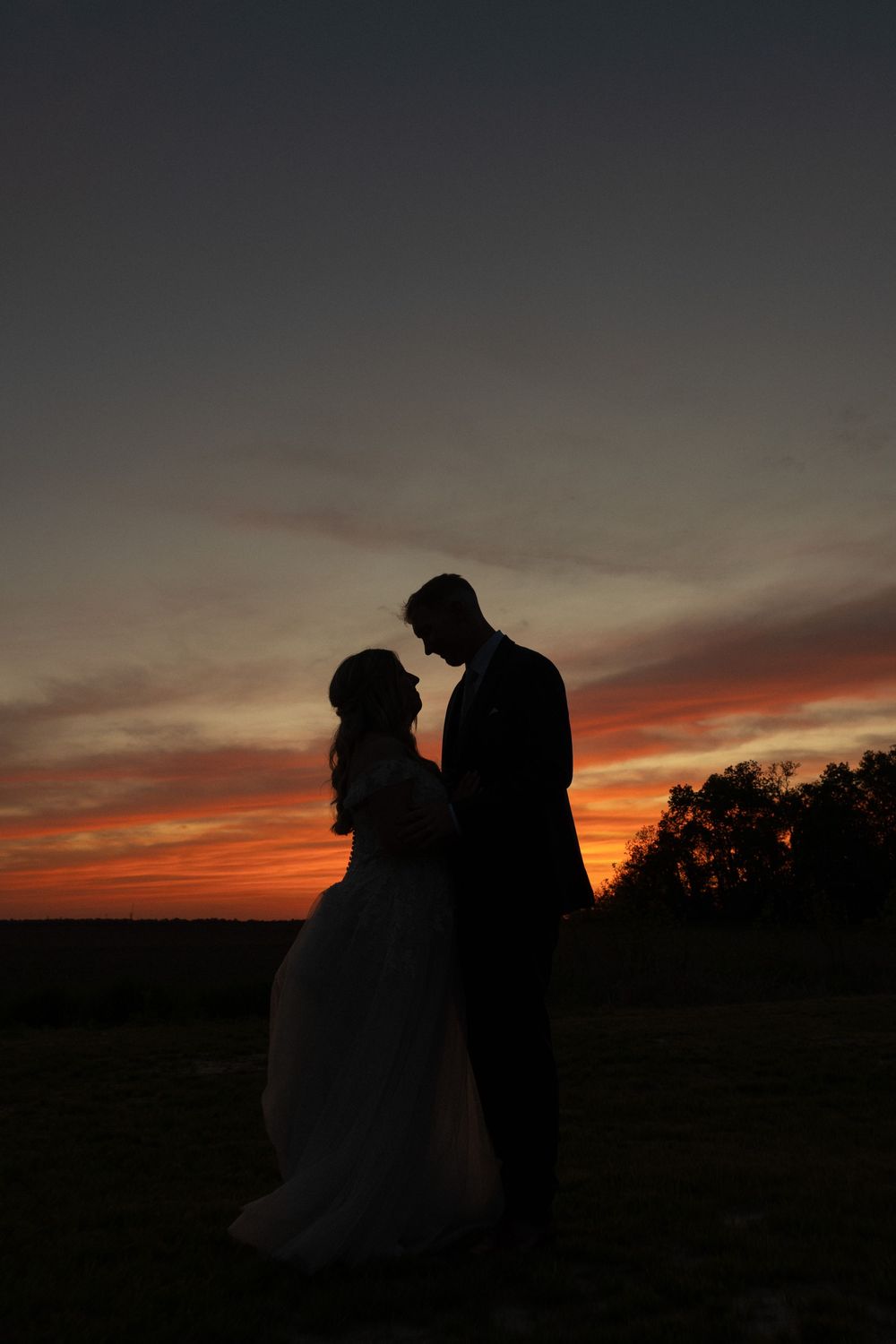 A romantic silhouette of a bride and groom standing together against a vibrant sunset sky.