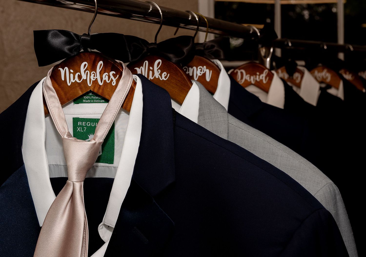Navy suits and blush tie on wooden hangers with personalized name tags.