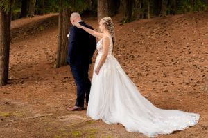 A romantic wedding couple shares a dance on a forest path with a flowing white dress and navy suit.
