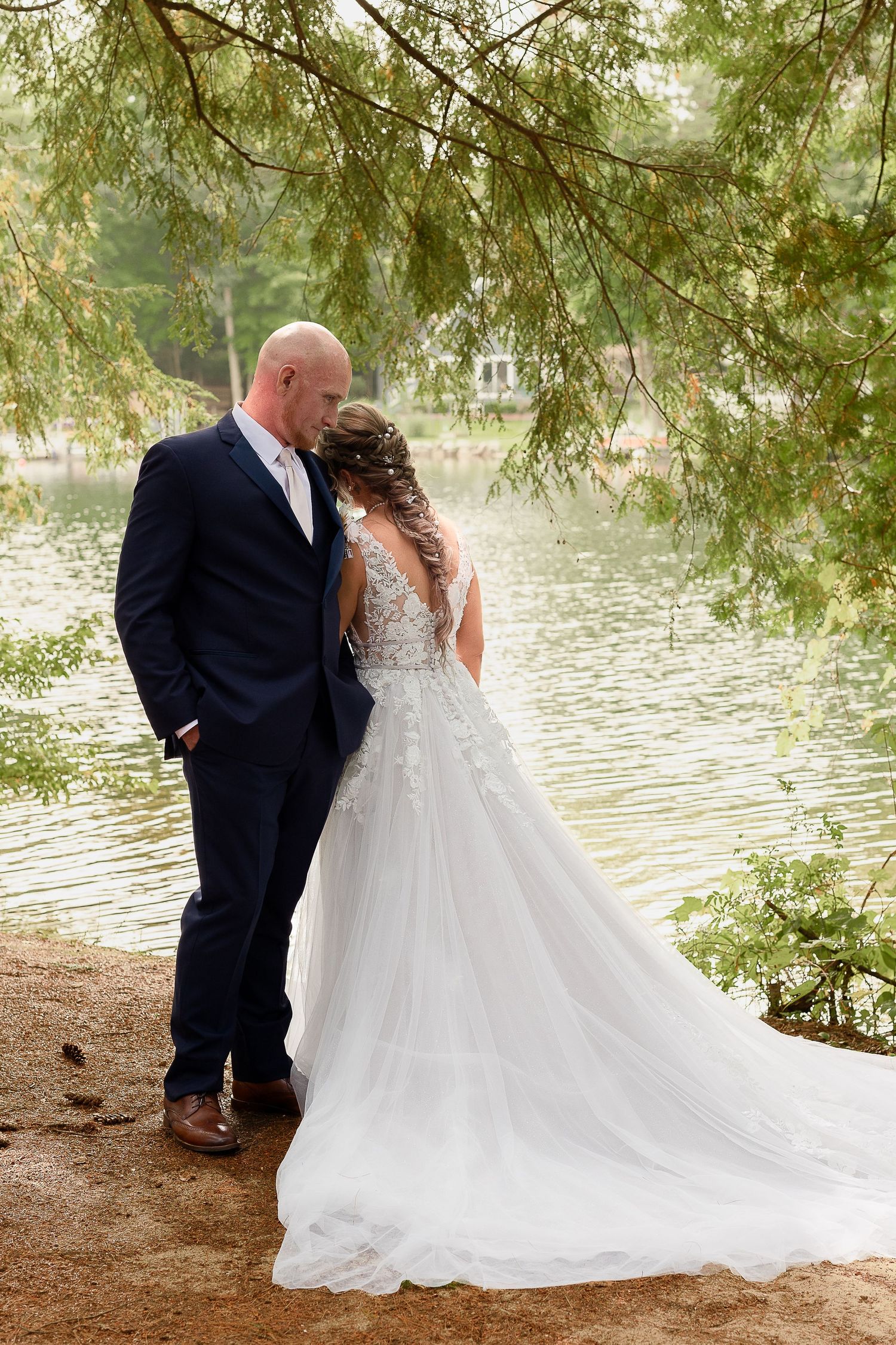 A tender moment between newlyweds by a serene lake with pine trees in the background.