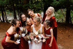Candid moment of bridal party laughing together in burgundy dresses against forest backdrop.